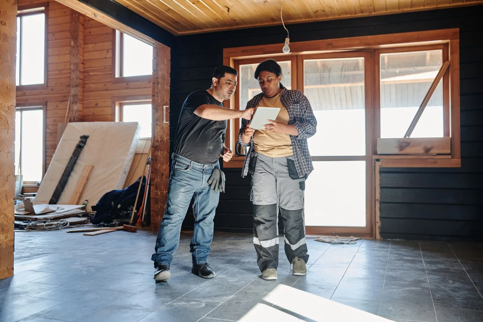Two construction workers inside a house reviewing plans on a digital tablet